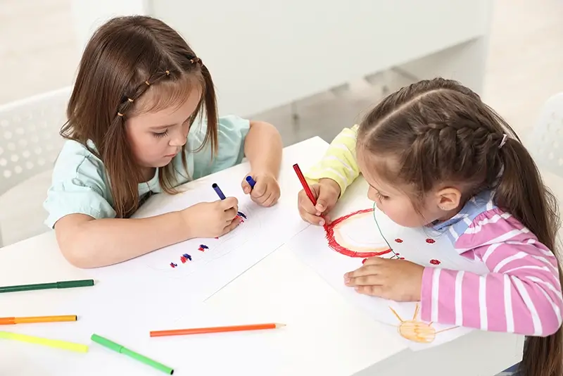 Two young girls drawing on paper with crayons
